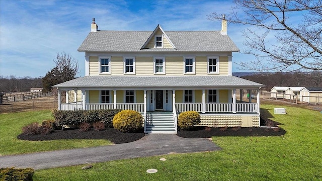 country-style home featuring covered porch, a shingled roof, a front lawn, and fence