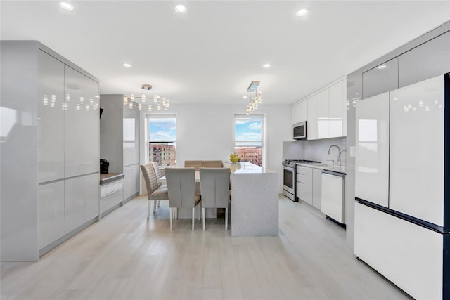 kitchen with light wood-type flooring, light countertops, appliances with stainless steel finishes, white cabinets, and modern cabinets