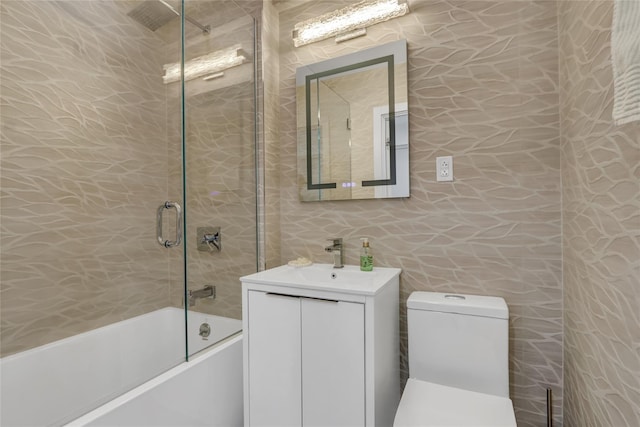 bathroom featuring vanity, tile walls, toilet, and shower / bath combination with glass door
