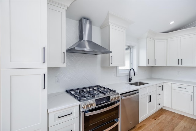 kitchen with light wood-type flooring, a sink, white cabinets, appliances with stainless steel finishes, and wall chimney exhaust hood
