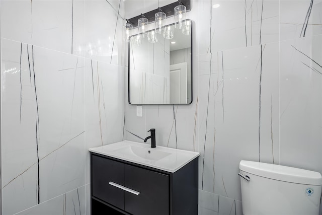 bathroom with toilet, vanity, and tile walls
