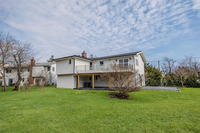 rear view of house with stucco siding, a chimney, a wooden deck, and a yard