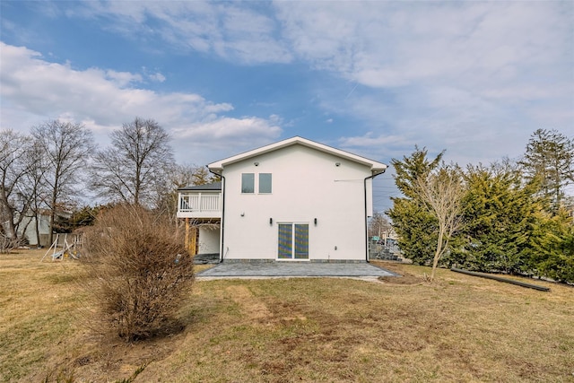 rear view of house with stucco siding, a balcony, a lawn, and a patio area