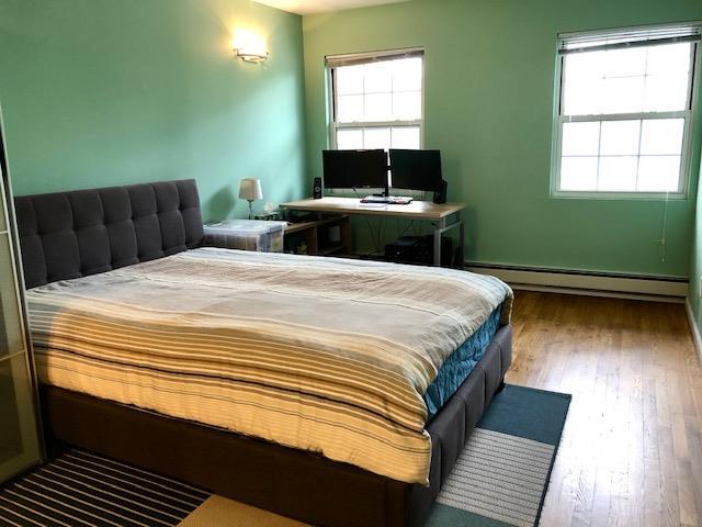 12-31 Robin Ln Unit 52L, Bayside, NY 11360 - bedroom featuring baseboard heating, multiple windows, and wood finished floors