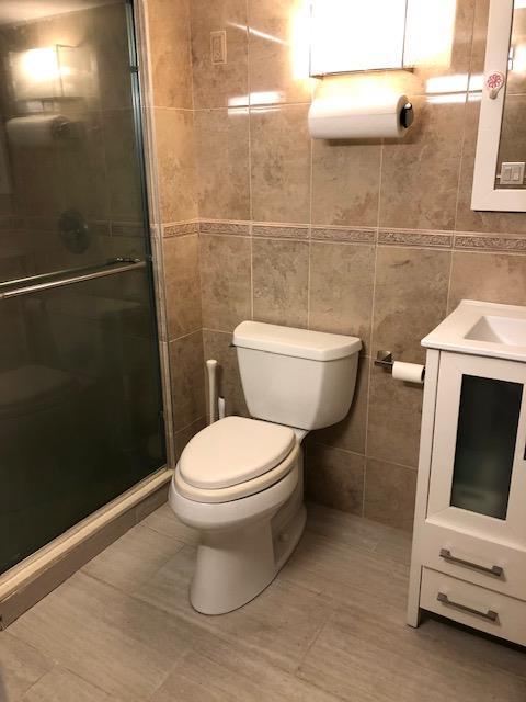 12-31 Robin Ln Unit 52L, Bayside, NY 11360 - full bath with tile walls, toilet, a shower stall, vanity, and tile patterned floors