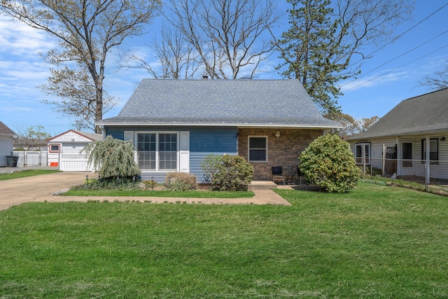view of front of home with roof with shingles, fence, an outbuilding, and a front yard