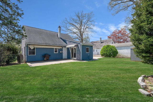 rear view of property with a shingled roof, a patio area, fence, and a yard