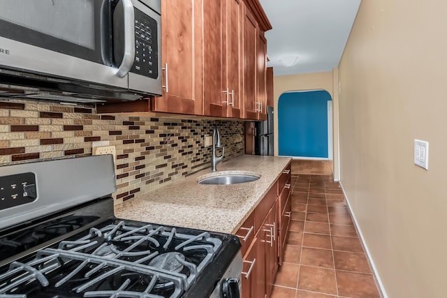 kitchen with brown cabinetry, dark tile patterned flooring, a sink, stainless steel appliances, and backsplash