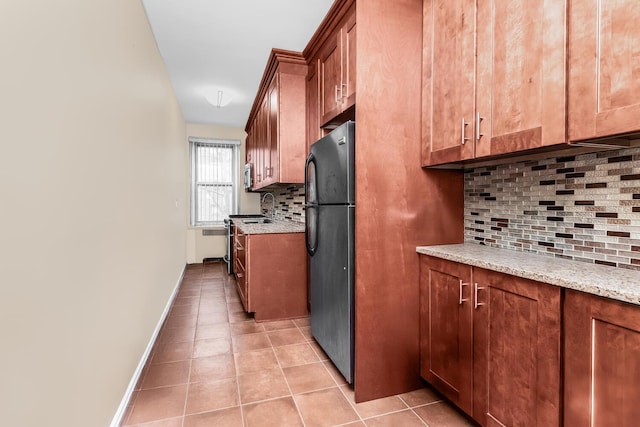 kitchen featuring brown cabinets, a sink, tasteful backsplash, freestanding refrigerator, and light tile patterned floors