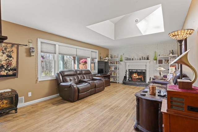living area with light wood-type flooring, a skylight, brick wall, baseboards, and a brick fireplace