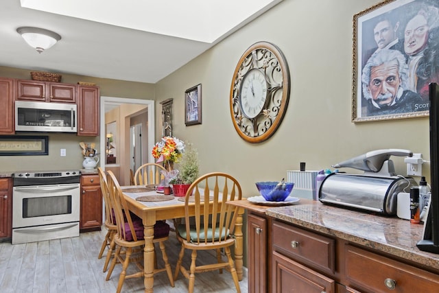 kitchen with dark brown cabinets, light stone countertops, light wood-type flooring, and stainless steel appliances