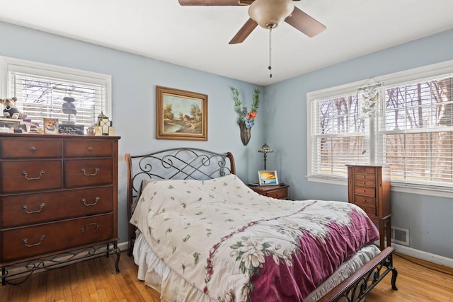 bedroom with light wood finished floors, visible vents, a ceiling fan, and baseboards
