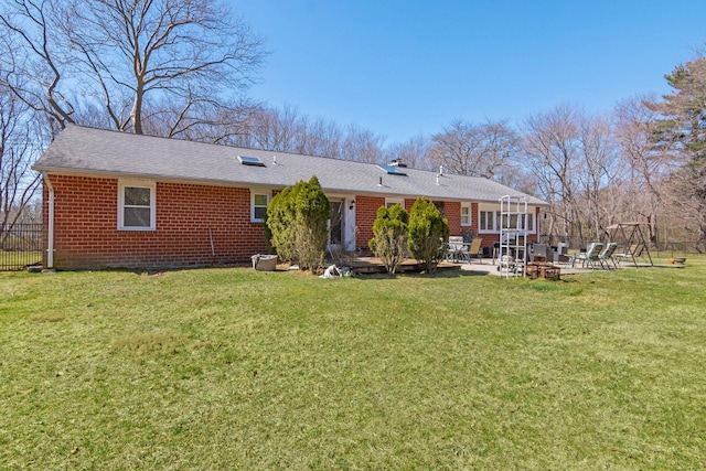 rear view of house featuring a patio, a yard, brick siding, and roof with shingles