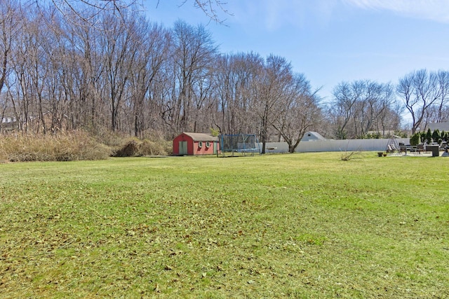 view of yard with a storage shed, a trampoline, an outdoor structure, and fence