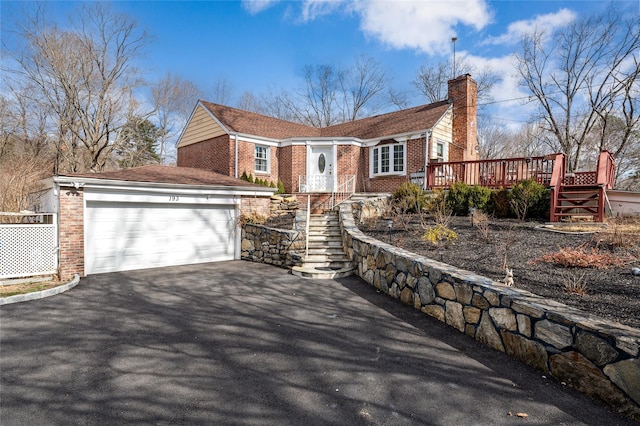 ranch-style house with aphalt driveway, a wooden deck, a chimney, brick siding, and a garage