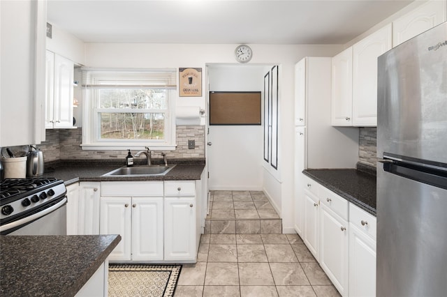 kitchen featuring tasteful backsplash, stainless steel appliances, white cabinets, dark countertops, and a sink
