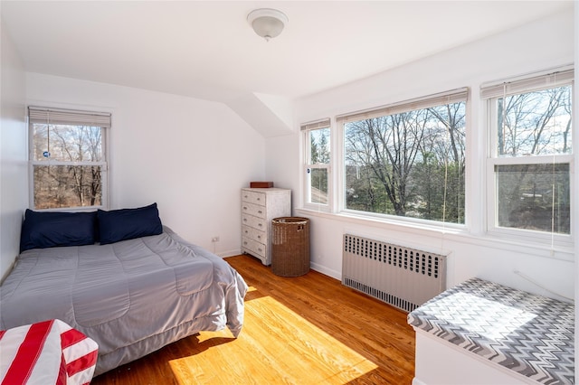 bedroom with multiple windows, wood finished floors, baseboards, and radiator