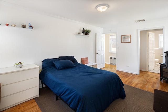 bedroom with radiator, crown molding, visible vents, baseboards, and wood finished floors