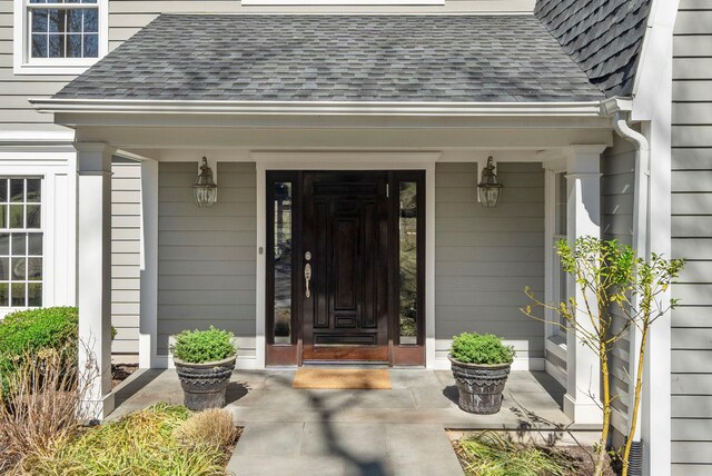 doorway to property with a porch and a shingled roof