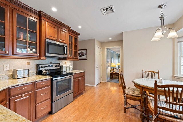 14 Hillside Ave, Saint James, NY 11780 - kitchen featuring stainless steel appliances, light wood-style floors, tasteful backsplash, brown cabinetry, and hanging light fixtures