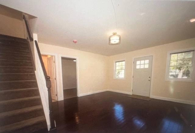 foyer entrance featuring dark wood finished floors, stairs, and baseboards