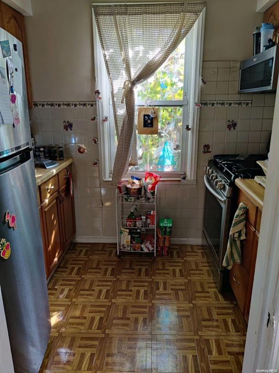 133-25 Blossom Ave, Flushing, NY 11355 - kitchen with brown cabinetry, appliances with stainless steel finishes, tile walls, and light countertops