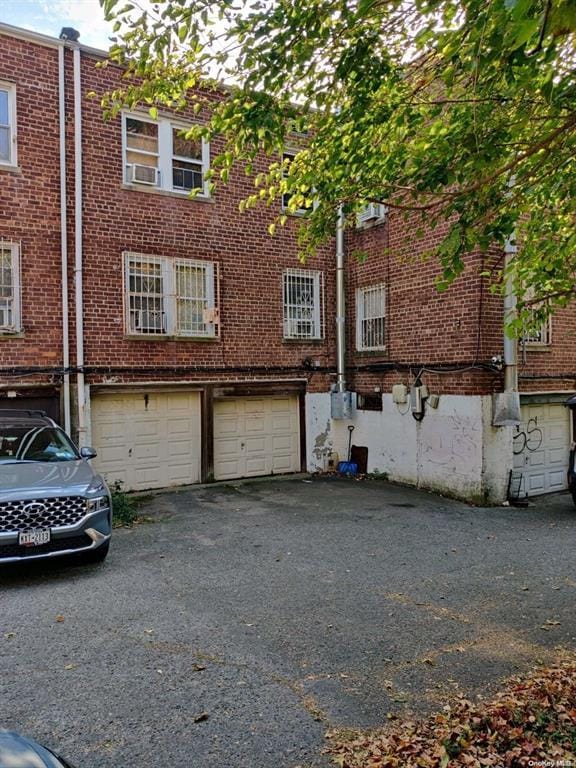 133-25 Blossom Ave, Flushing, NY 11355 - back of house featuring brick siding, an attached garage, and driveway