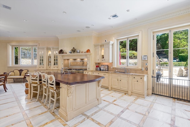 186 Kings Point Rd, Great Neck, NY 11024 - kitchen with inlaid floor details, cream cabinets, a sink, glass insert cabinets, and a kitchen island with sink