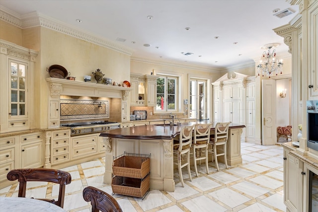 186 Kings Point Rd, Great Neck, NY 11024 - kitchen featuring cream cabinets, inlaid floor details, stainless steel gas stovetop, a breakfast bar, and a center island with sink