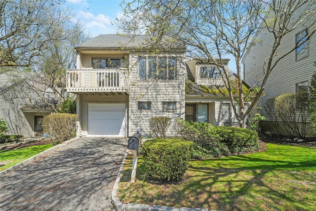 view of front of house with a garage, a balcony, driveway, and a front lawn