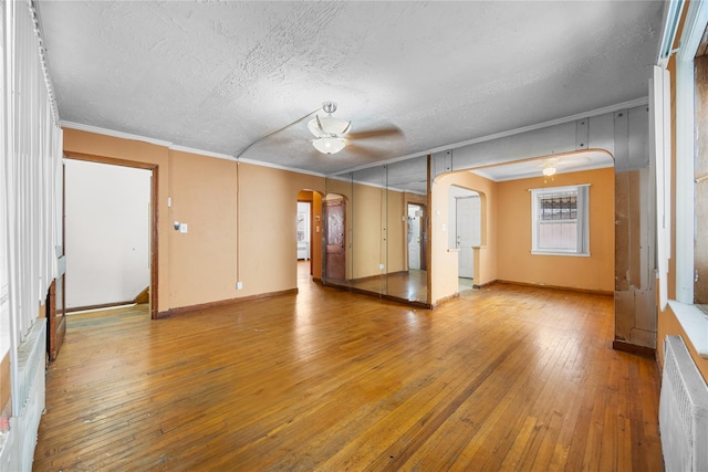unfurnished living room with arched walkways, hardwood / wood-style flooring, a ceiling fan, and crown molding