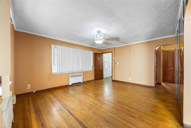 unfurnished room with arched walkways, radiator, wood-type flooring, and ornamental molding