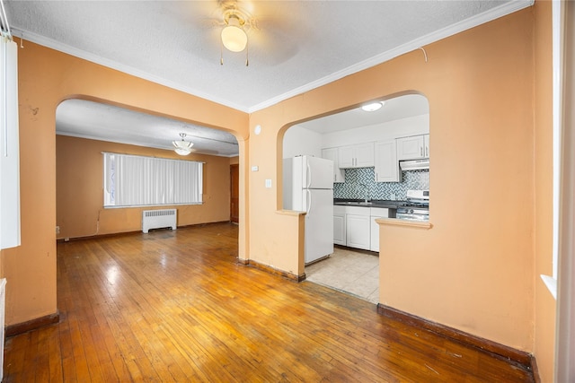 interior space with crown molding, radiator heating unit, a ceiling fan, and arched walkways