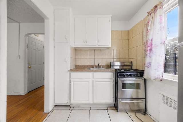 kitchen featuring stainless steel range with gas stovetop, radiator heating unit, decorative backsplash, white cabinets, and a sink