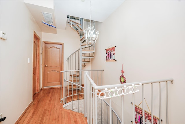 corridor with an upstairs landing, visible vents, a chandelier, baseboards, and wood finished floors