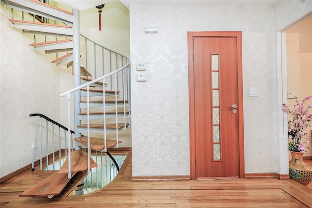 staircase featuring baseboards, wallpapered walls, and wood finished floors
