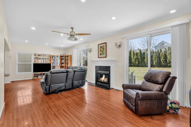 living room with a glass covered fireplace, recessed lighting, a ceiling fan, and wood-type flooring