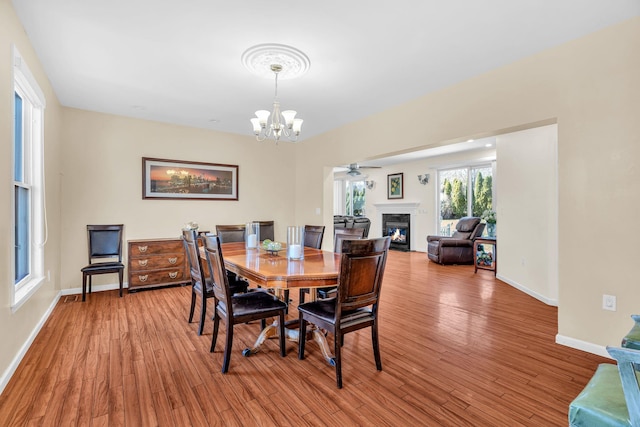 dining area featuring baseboards, wood finished floors, a glass covered fireplace, and ceiling fan with notable chandelier