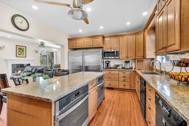 kitchen featuring a ceiling fan, a sink, light wood-style floors, appliances with stainless steel finishes, and light stone countertops