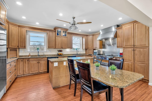kitchen with a kitchen bar, light wood-type flooring, a sink, a center island, and wall chimney exhaust hood