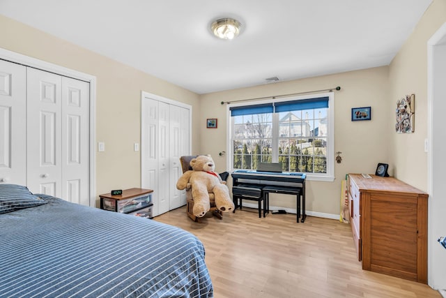 bedroom with light wood-type flooring, baseboards, two closets, and visible vents