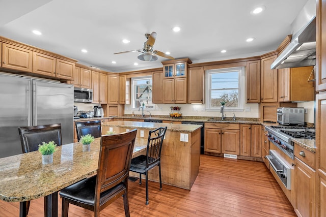 kitchen featuring a warming drawer, a breakfast bar, appliances with stainless steel finishes, wall chimney range hood, and ceiling fan
