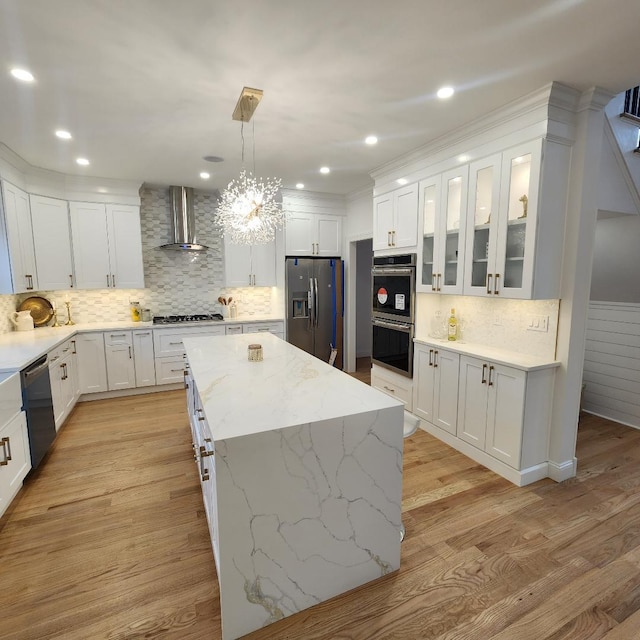 kitchen with wall chimney range hood, decorative backsplash, a kitchen island, white cabinets, and stainless steel appliances
