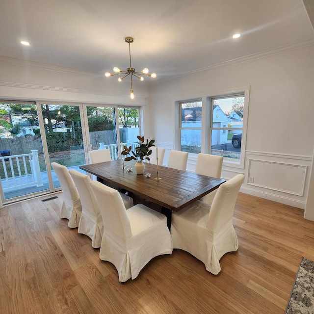dining space with light wood-style floors, ornamental molding, wainscoting, and a chandelier