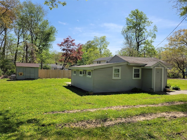 rear view of property with an outbuilding, a yard, a storage shed, and fence