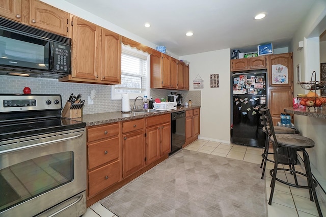 kitchen featuring brown cabinets, black appliances, a sink, backsplash, and light tile patterned flooring