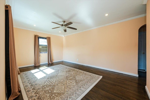 empty room with arched walkways, dark wood finished floors, crown molding, and ceiling fan