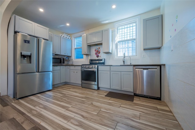 kitchen with wood finish floors, a sink, recessed lighting, arched walkways, and appliances with stainless steel finishes