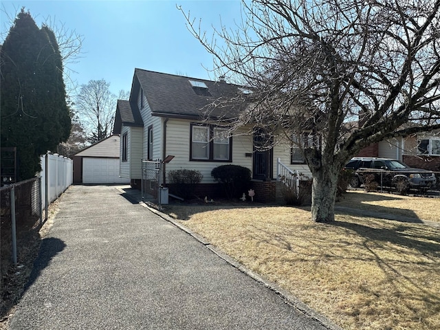 view of front of home featuring a front yard, fence, roof with shingles, an outdoor structure, and a detached garage