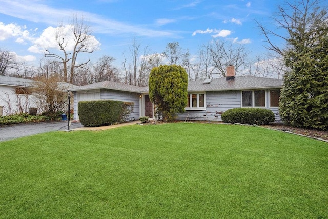ranch-style house featuring a chimney, aphalt driveway, a garage, and a front lawn